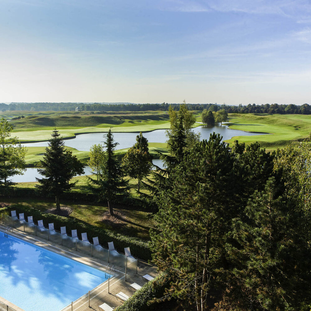 a swimming pool surrounded by chairs and trees with a golf course in the background
