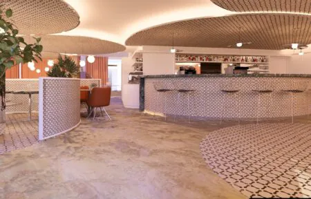 en::Bar with rounded shapes from ceiling to floor, ceiling and counter patterns echoed on the floor, metal bar stools, and soft, luminous colors. fr::Bar aux formes arrondies du plafond au sol, motifs du plafond et du comptoir repris au sol, fauteuils de bar métalliques, couleurs douces et lumineuses.