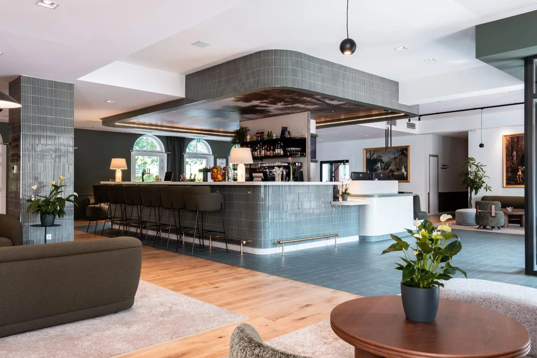 en::hotel lobby and reception with a central tiled bar, artistic ceiling painting, lounge seating, and access to the garden terrace fr::lobby de l’hôtel avec réception autour d’un bar central carrelé, peinture artistique au plafond, assises lounge et accès à la terrasse sur jardin