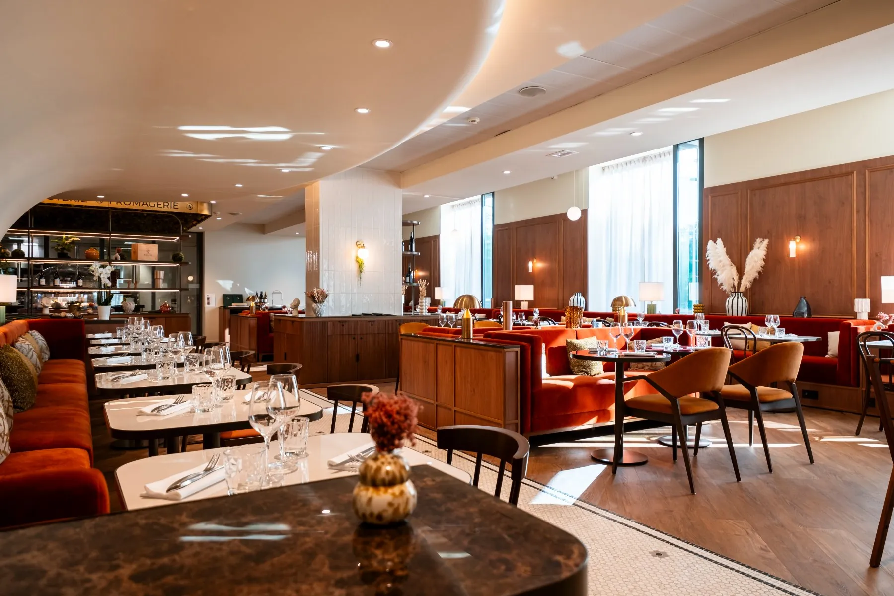 une salle de restaurant élégante avec tables dressées, murs blancs et bois, banquettes et chaises en bois