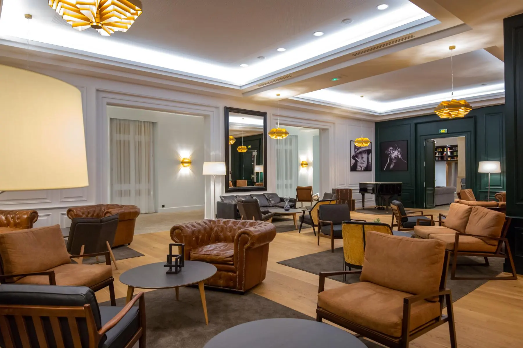 vue d’ensemble du bar de l’hôtel en soirée, avec jeux de lumières, piano, fauteuils et canapés en cuir, tables basses en bois