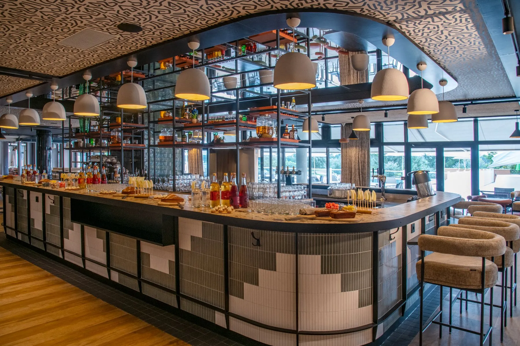 Bar central imposant et design, idéal pour une offre cocktail d’entreprise, situé au cœur du restaurant avec vue sur le parcours de golf et la piscine
