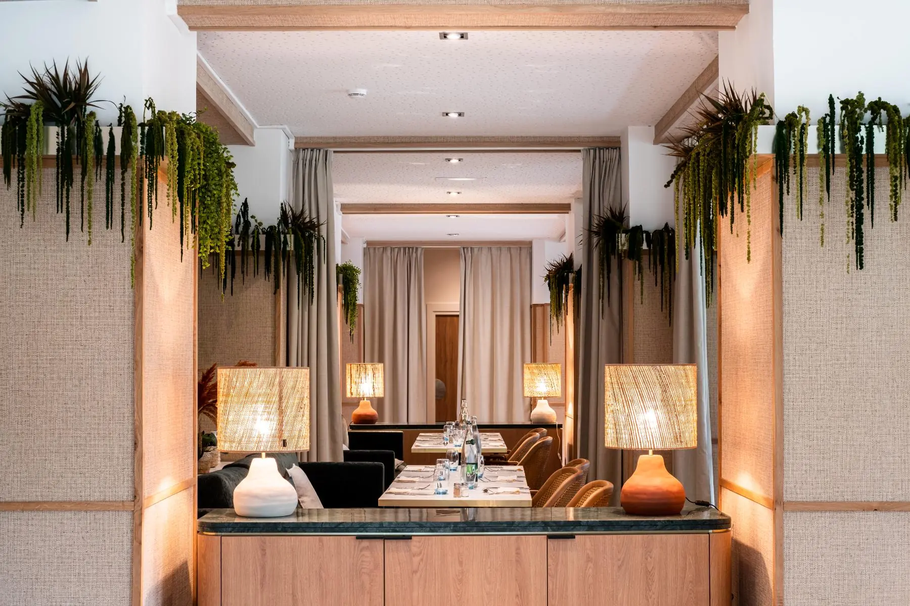 en::focus on a restaurant area with tables for two or four guests, offering a more intimate setting thanks to optional curtain dividers, framed by two plant-covered columns with natural materials fr::focus dans la salle de restaurant sur un espace avec tables de deux ou quatre personnes, offrant une ambiance plus intime grâce à des rideaux de séparation, encadré par deux colonnes végétalisées habillées de matières naturelles