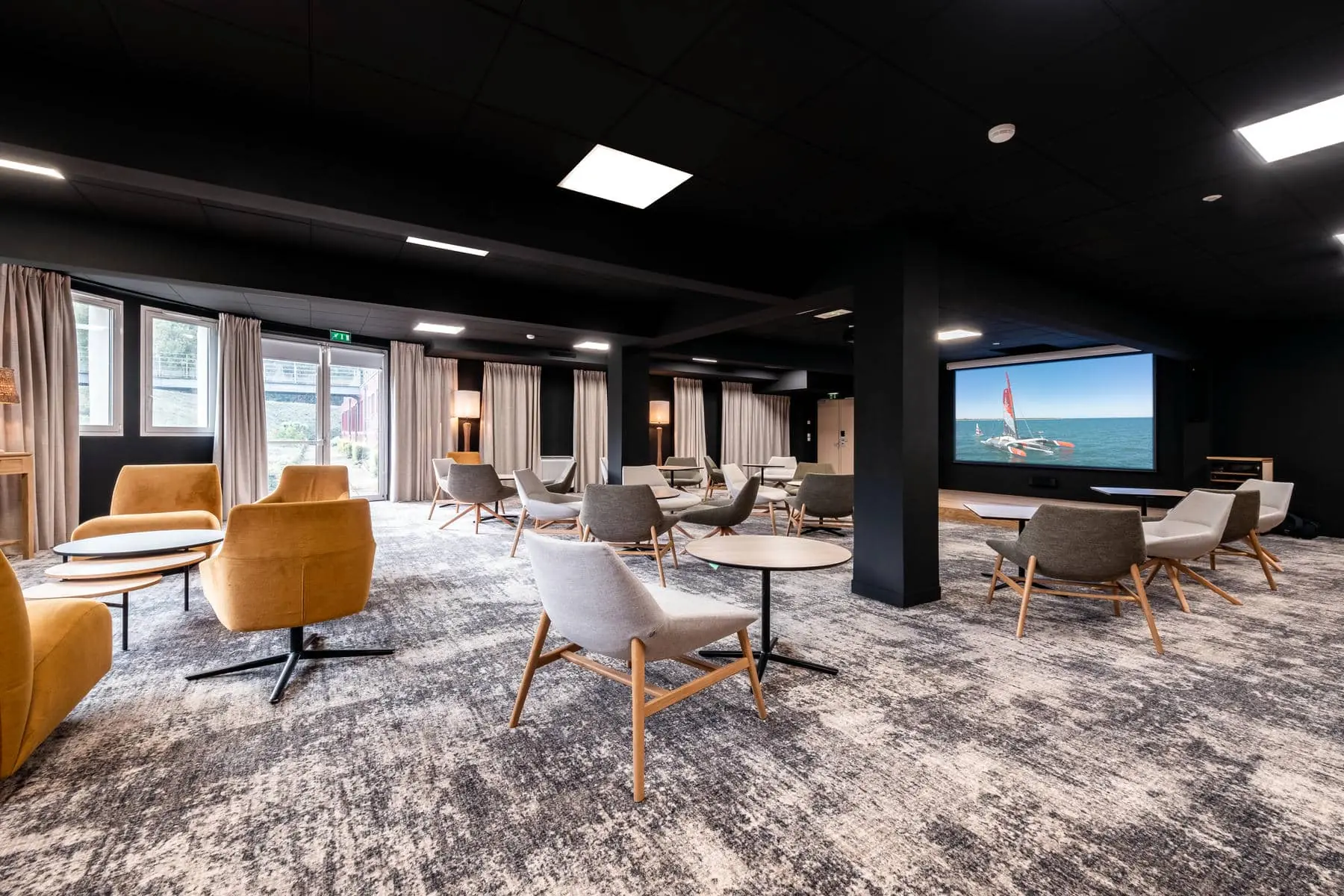 une salle avec des chaises et des tables et un grand écran sur lequel figure un voilier