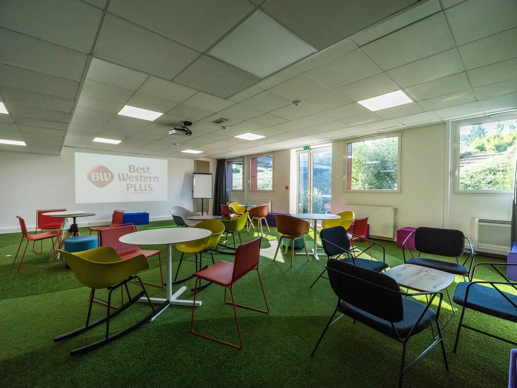 une salle avec des tables et des chaises et un écran de projection sur lequel est inscrit "Best Western Plus"