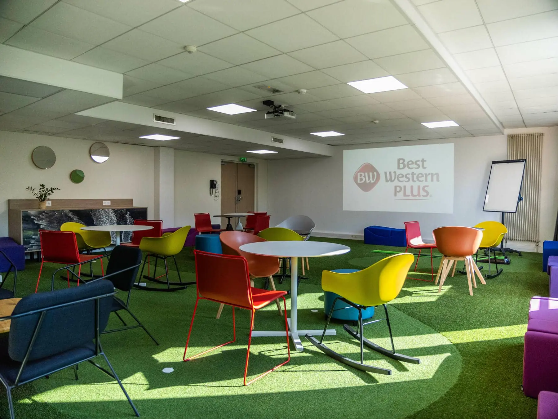 une salle avec des tables et des chaises et un écran de projection sur lequel est inscrit "Best Western Plus"