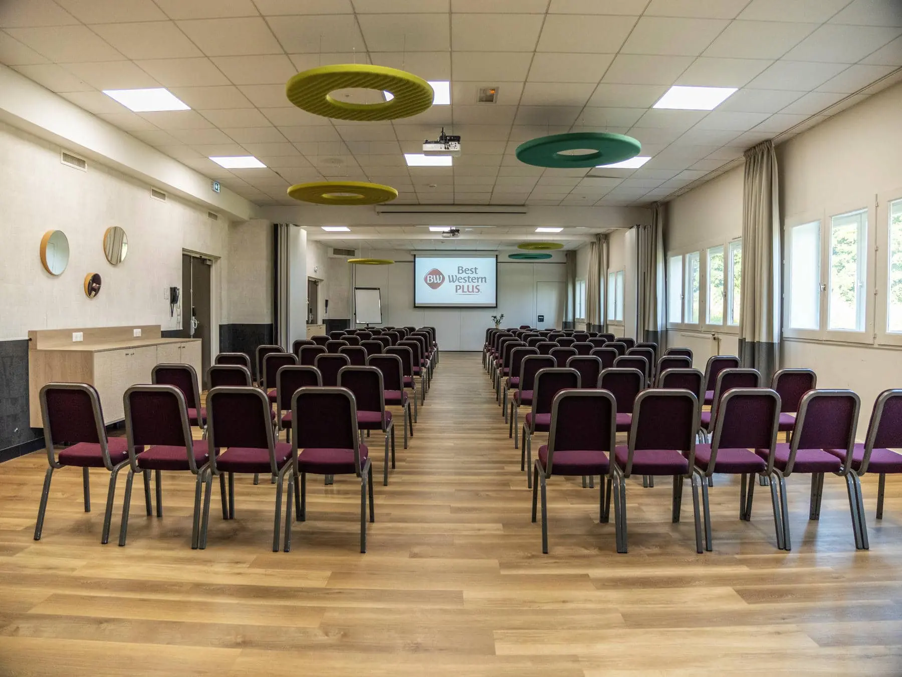 une grande salle avec des rangées de chaises et un écran de projection sur lequel est inscrit "best western plus"