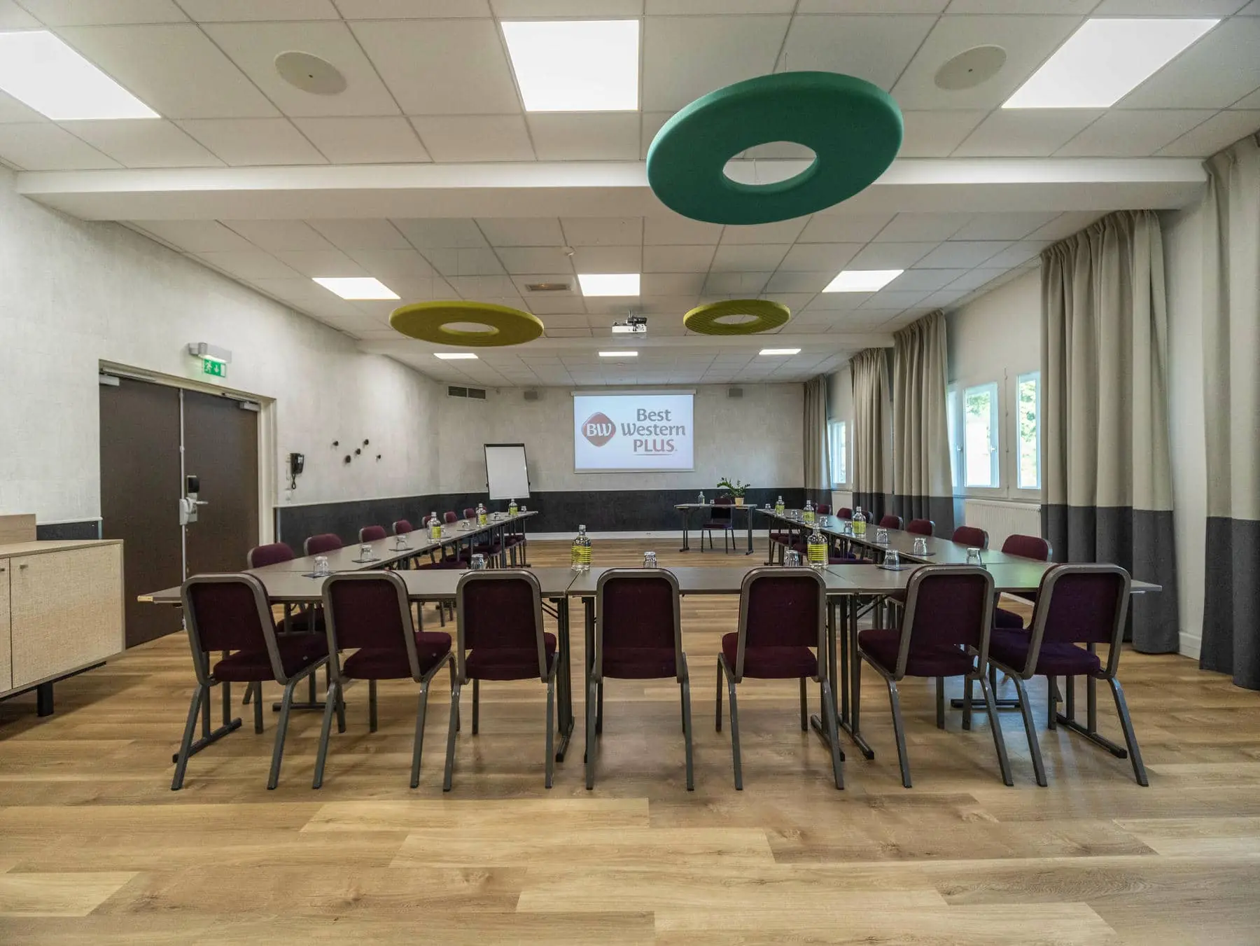 une salle de conférence avec des tables et des chaises et un écran de projection sur lequel est inscrit "Best Western Plus"