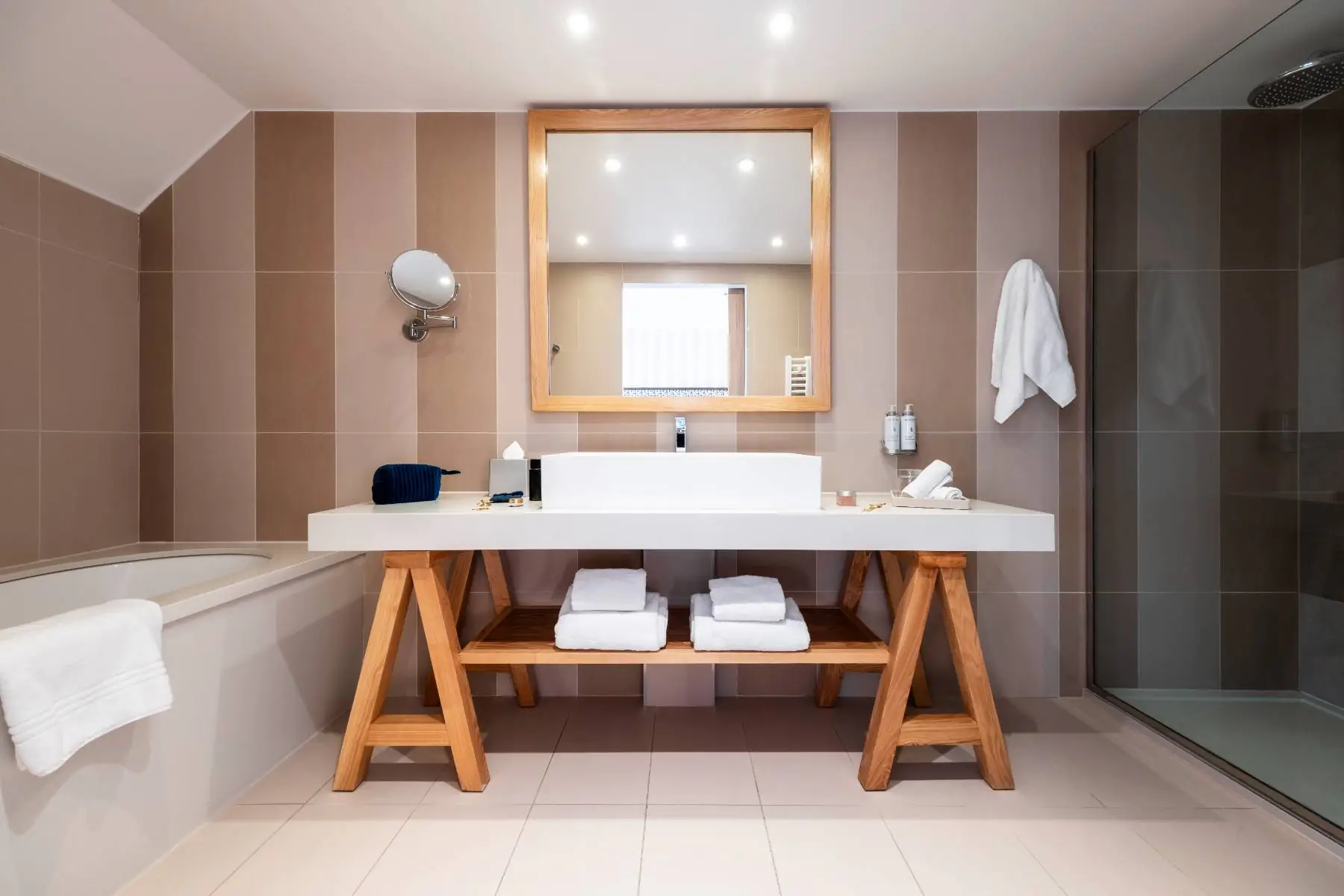 en::Modern bathroom with shower, tiled walls, a large white sink, and wooden fittings in a clean, comfortable design. fr::Salle de bain moderne avec douche, carrelage mural, large lavabo blanc et aménagement en bois, au design épuré et confortable.