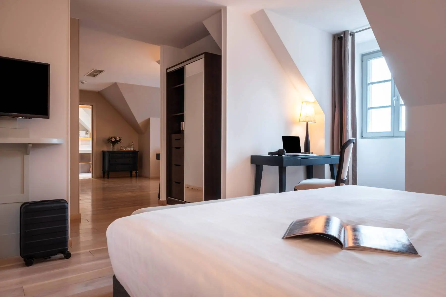 en::View from the double bed with the window and desk nearby, leading to the lounge area and the bathroom in the background. fr::Vue depuis le lit double avec fenêtre et bureau à proximité, ouvrant sur l’espace salon puis la salle de bain en arrière-plan.