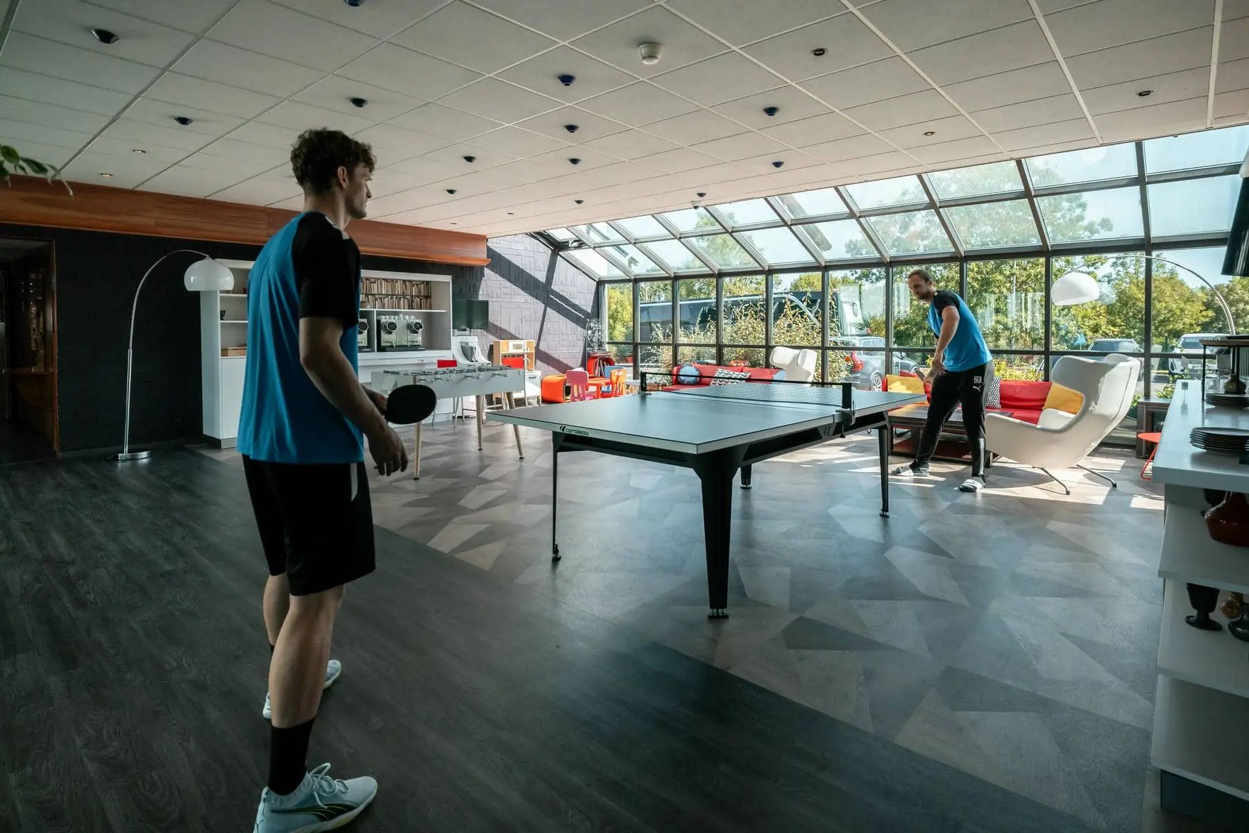 deux hommes jouent au ping-pong dans une grande salle