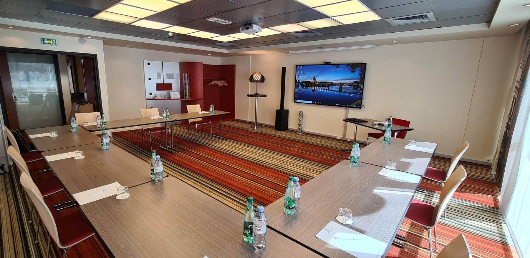 a conference room with tables and chairs and a large screen on the wall