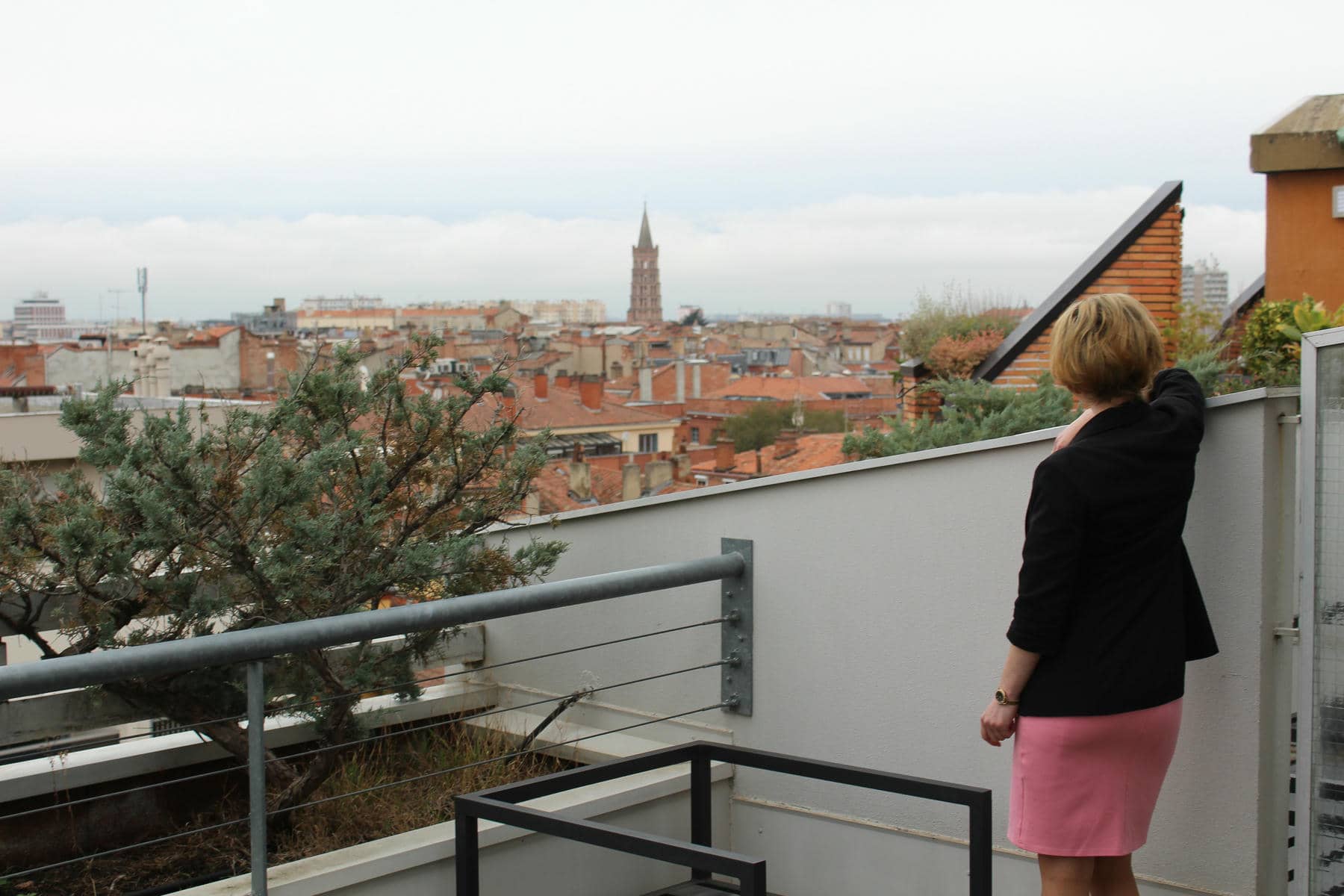 a woman in a pink skirt stands on a balcony overlooking a city