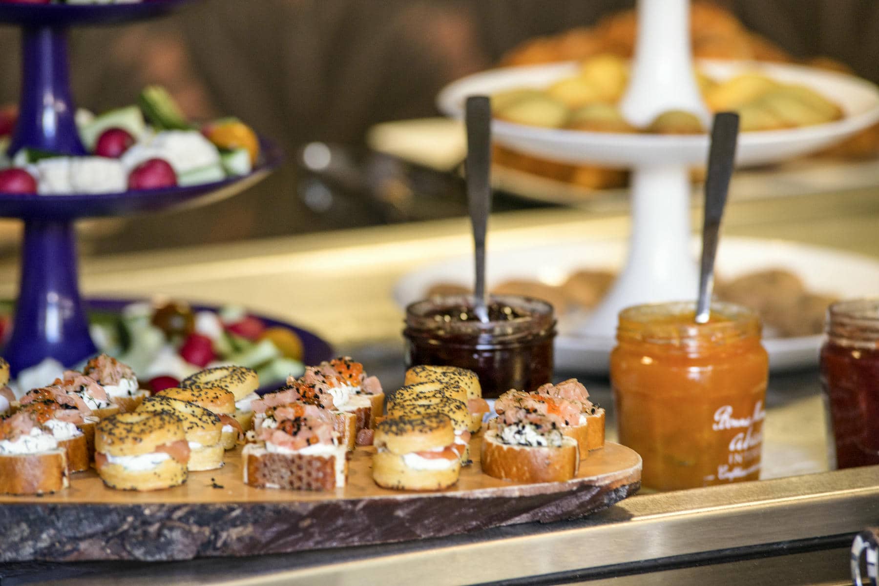 a wooden cutting board with appetizers on it next to jars of jam