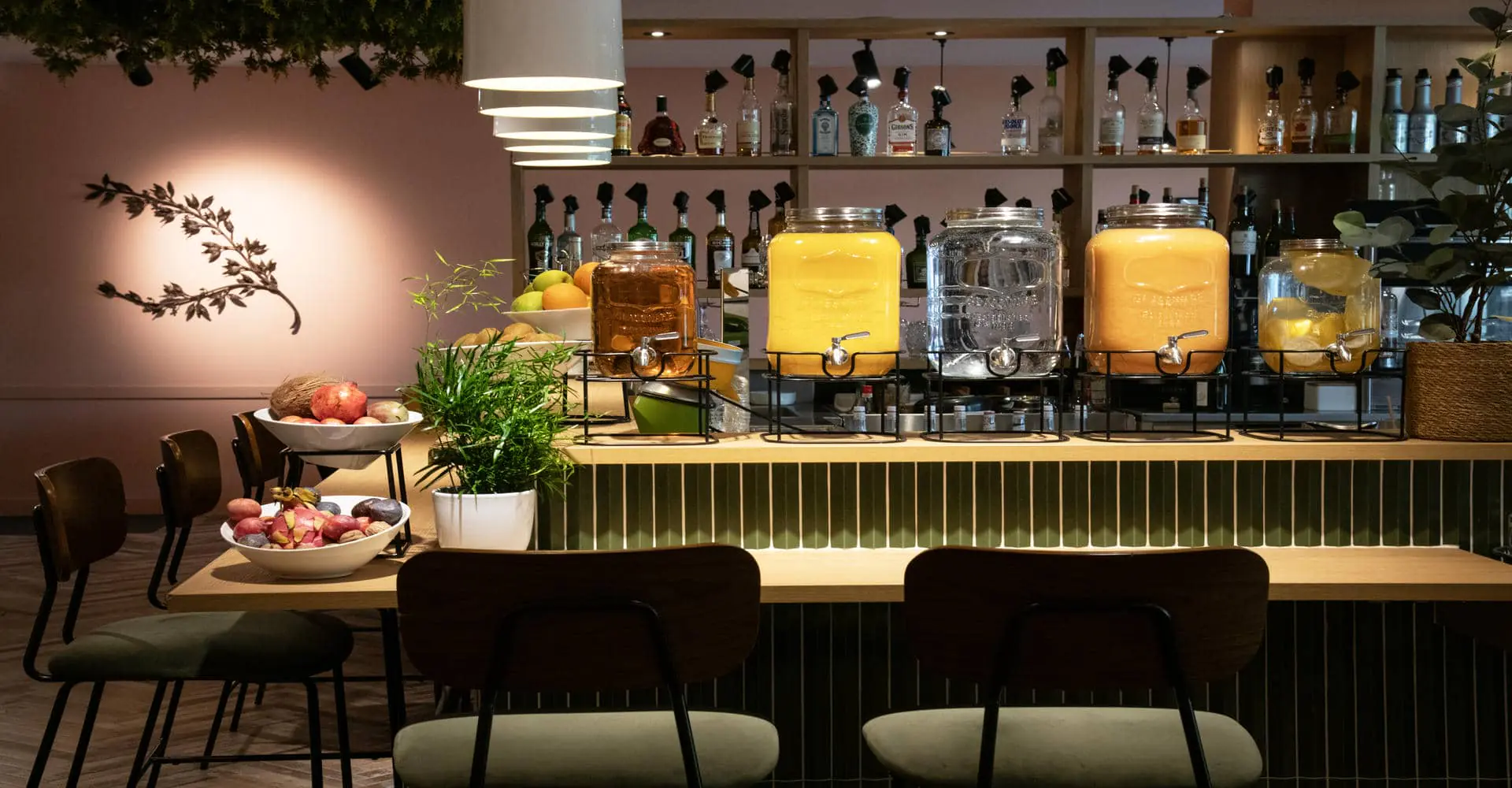 Un buffet petit-déjeuner dressé sur un bar avec bonbonnes en verre de différents jus et eaux, et des corbeilles de fruits frais.
