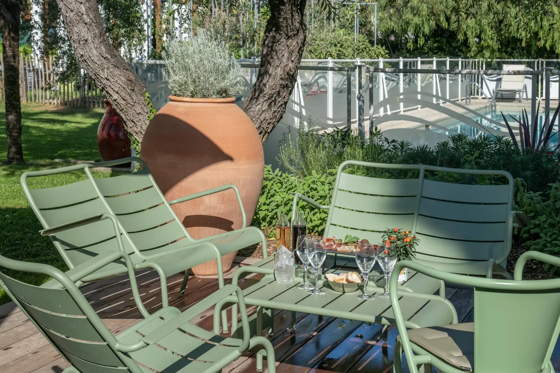 un patio avec des chaises vertes et une table sur laquelle sont posés des verres à vin