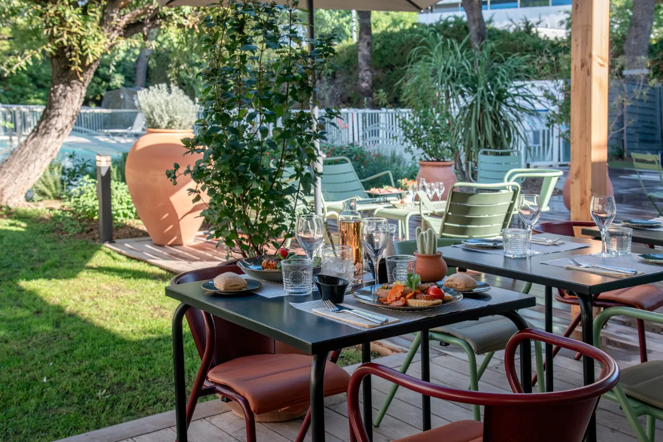 Green wooden terrace overlooking the hotel pool, with set tables and served dishes, ideal for a seminar meal.