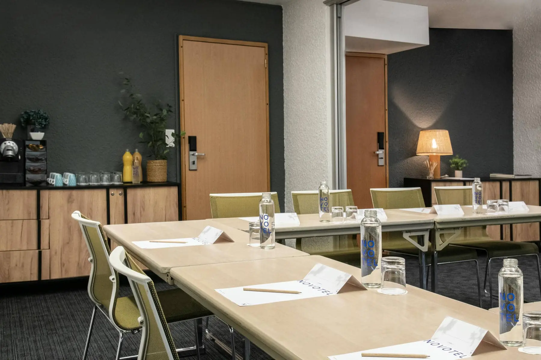 une salle de conférence aménagée avec des tables et des chaises et des bouteilles d'eau Novotel