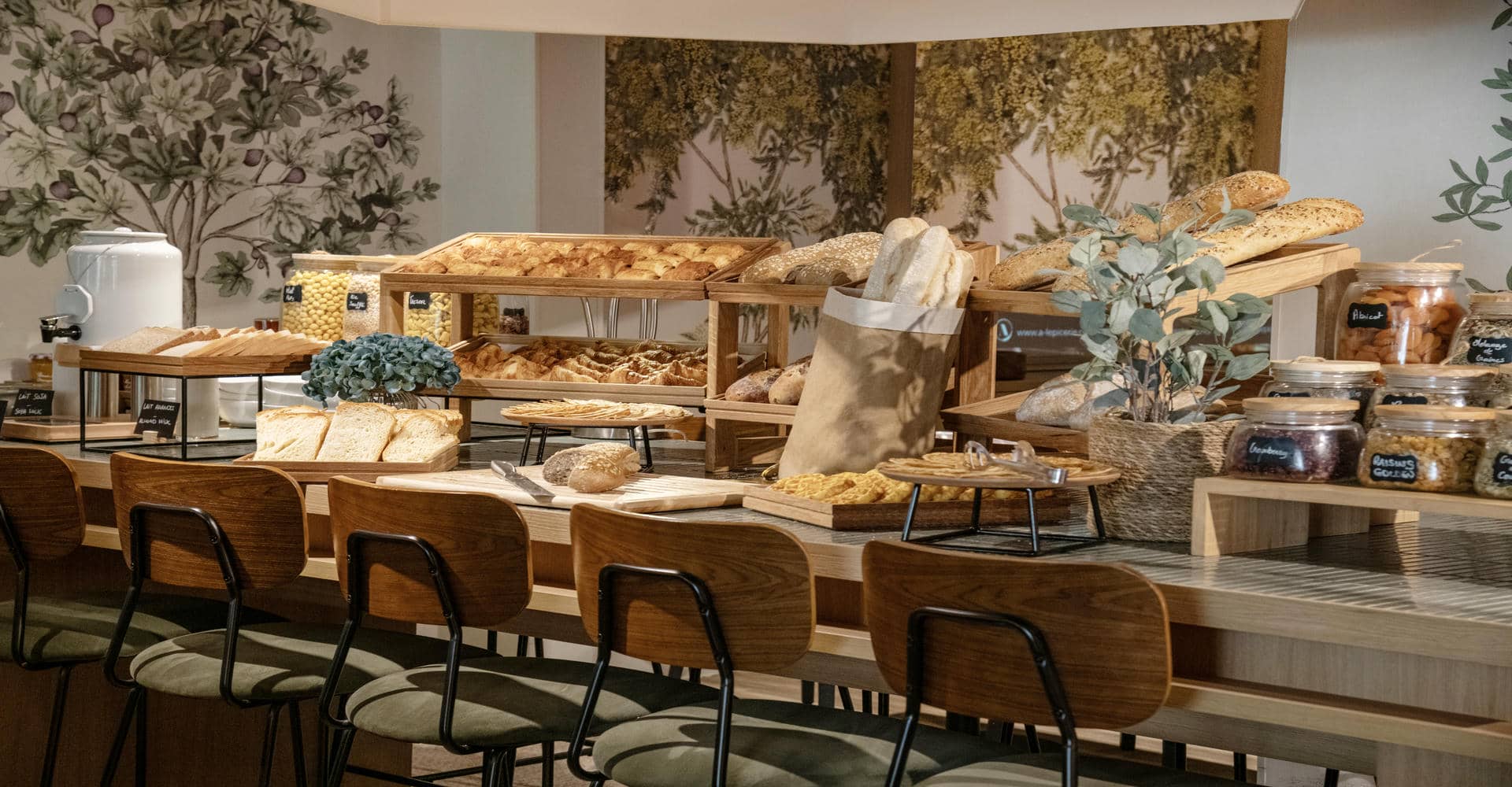 Un buffet petit-déjeuner garni de viennoiseries, différents pains et pots de céréales.