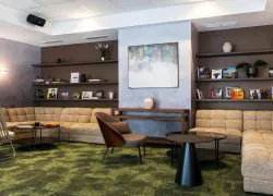 en::Books line elegant wall shelves around a corner sofa, armchairs, and green carpeting. A stylish seminar venue in Grenoble. fr::Des livres habillent de belles étagères murales autour d’un canapé d’angle, de fauteuils et d’une moquette verte. Un lieu séminaire Grenoble design.