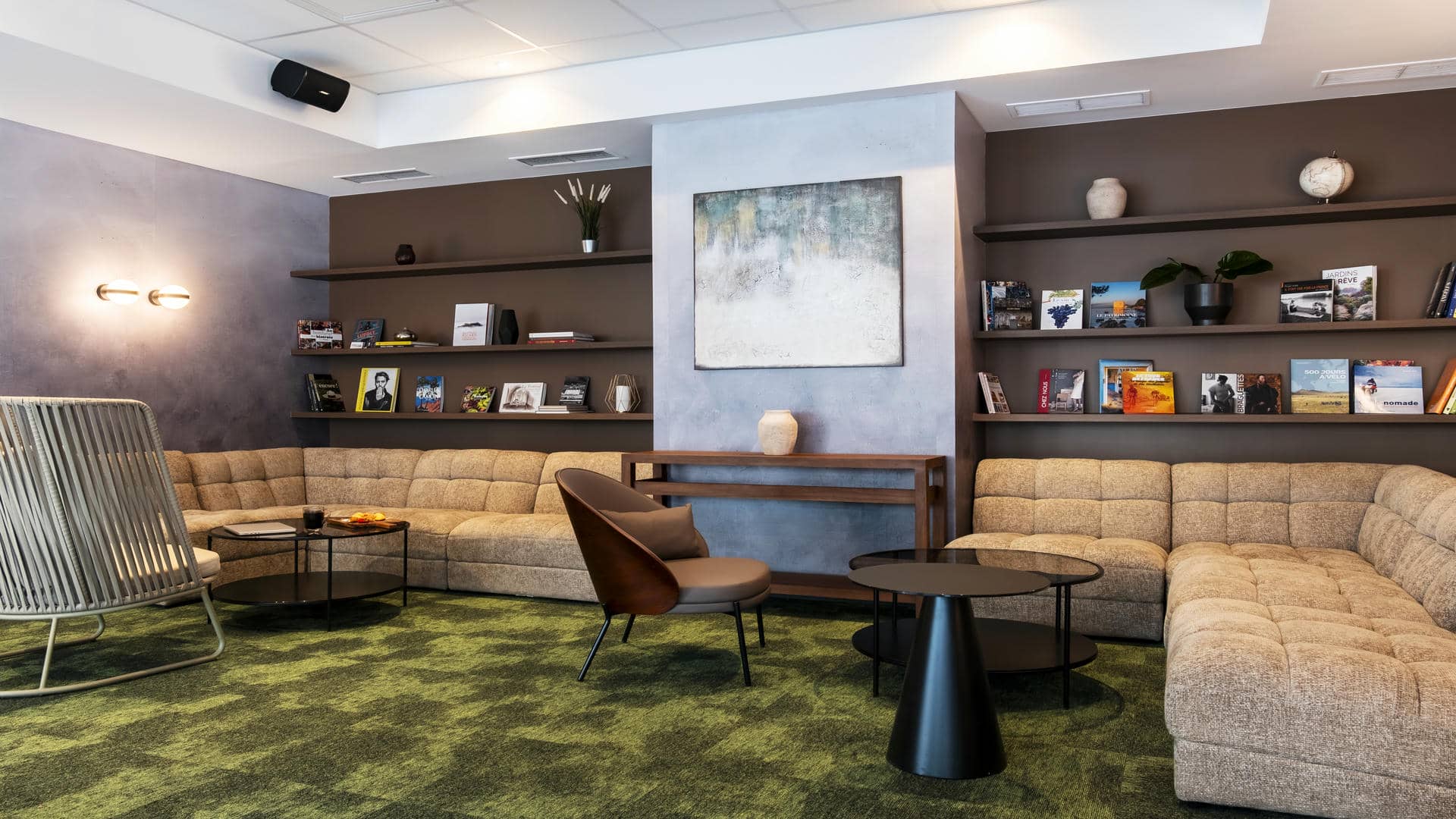 en::Books line elegant wall shelves around a corner sofa, armchairs, and green carpeting. A stylish seminar venue in Grenoble. fr::Des livres habillent de belles étagères murales autour d’un canapé d’angle, de fauteuils et d’une moquette verte. Un lieu séminaire Grenoble design.