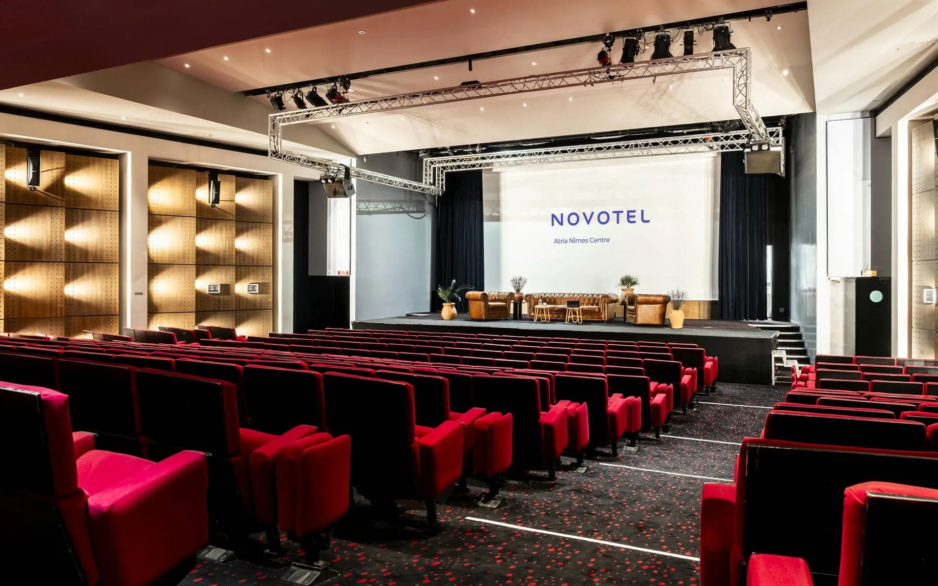 un grand auditorium avec des rangées de sièges rouges et un grand écran sur lequel est inscrit novotel