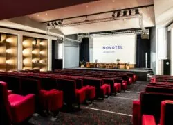 un grand auditorium avec des rangées de sièges rouges et un grand écran sur lequel est inscrit novotel