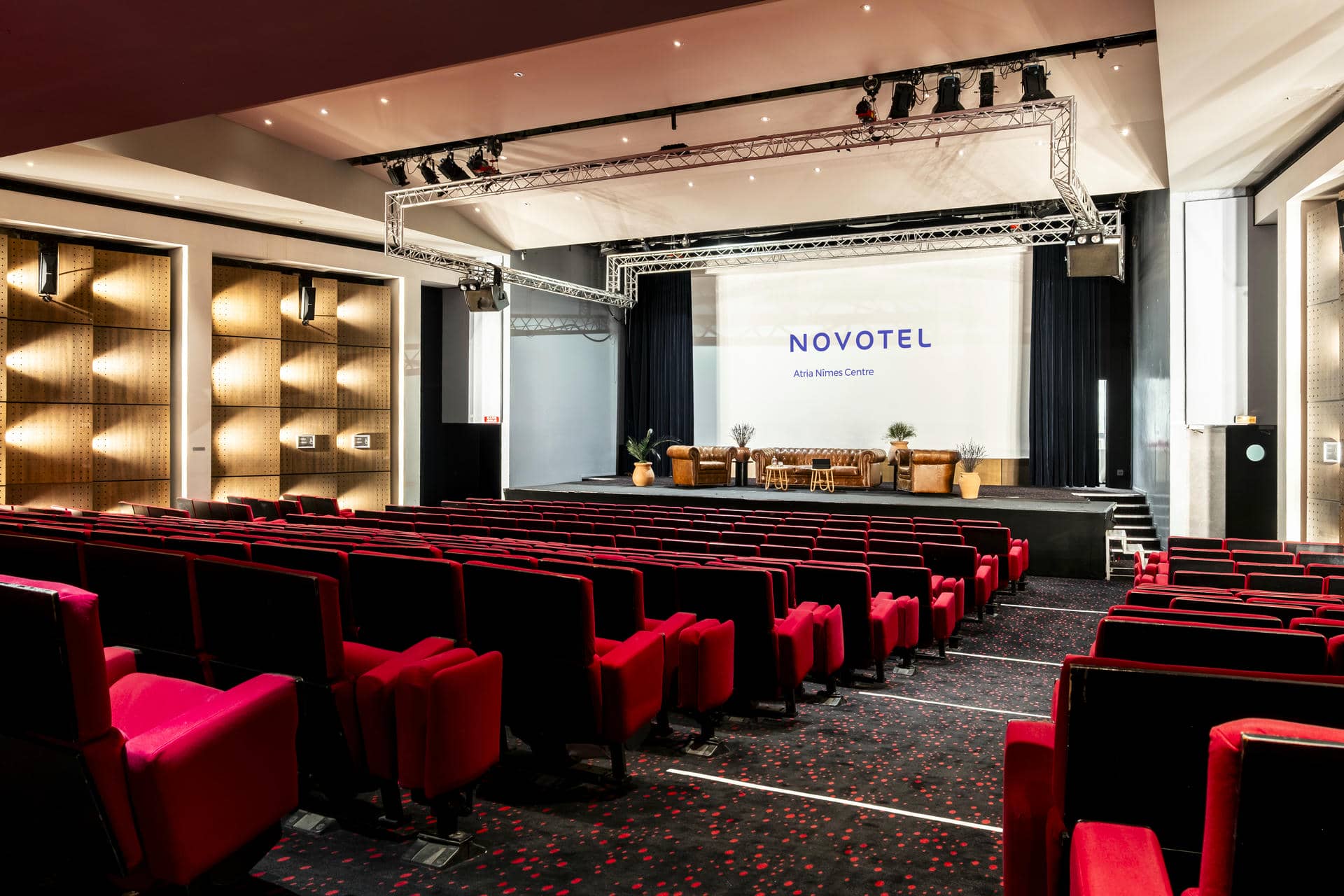 un grand auditorium avec des rangées de sièges rouges et un grand écran sur lequel est inscrit novotel