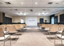 rows of wooden chairs in front of a projector screen that says novotel
