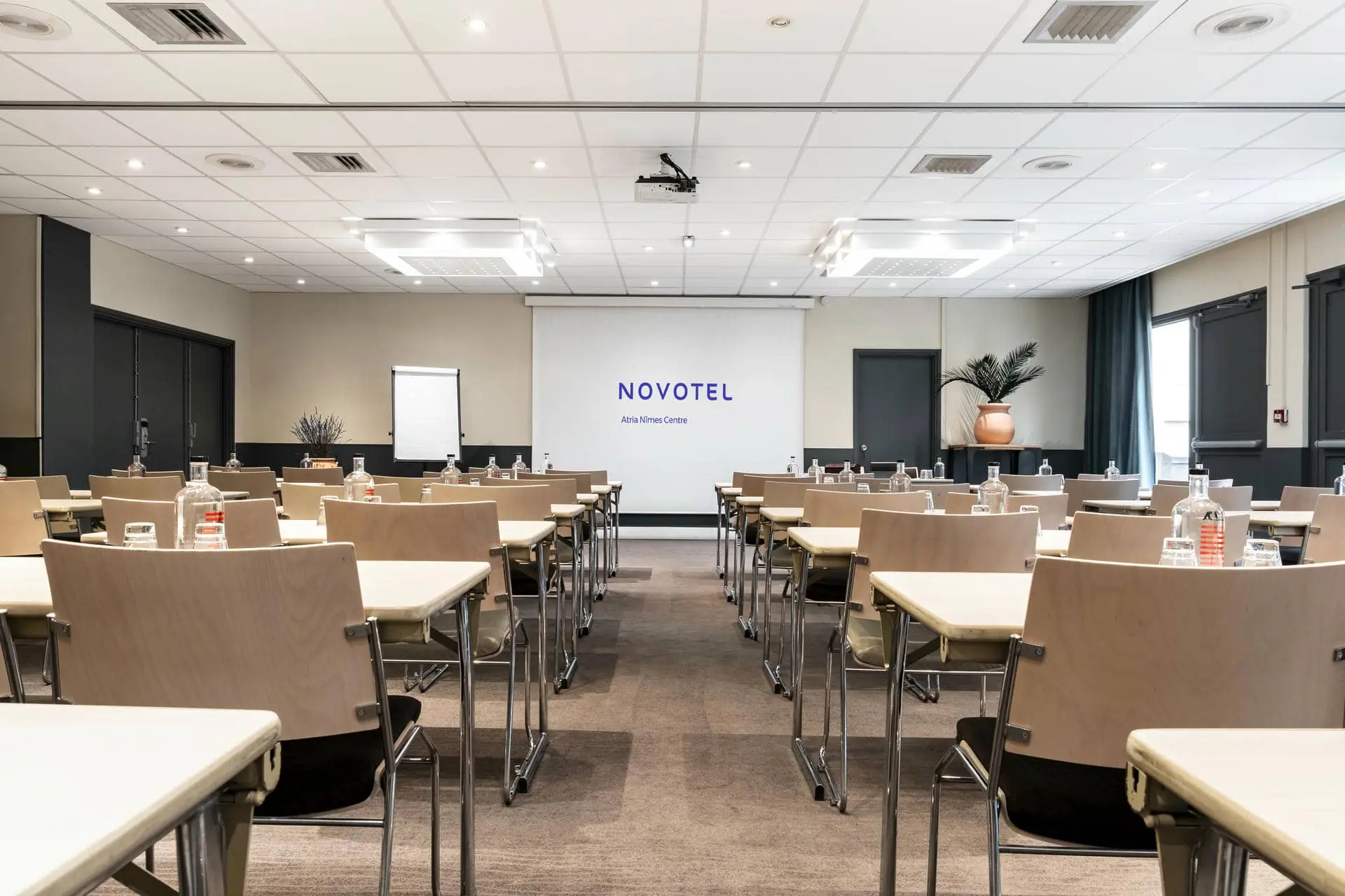 des rangées de tables et de chaises devant un écran de projection sur lequel est inscrit novotel