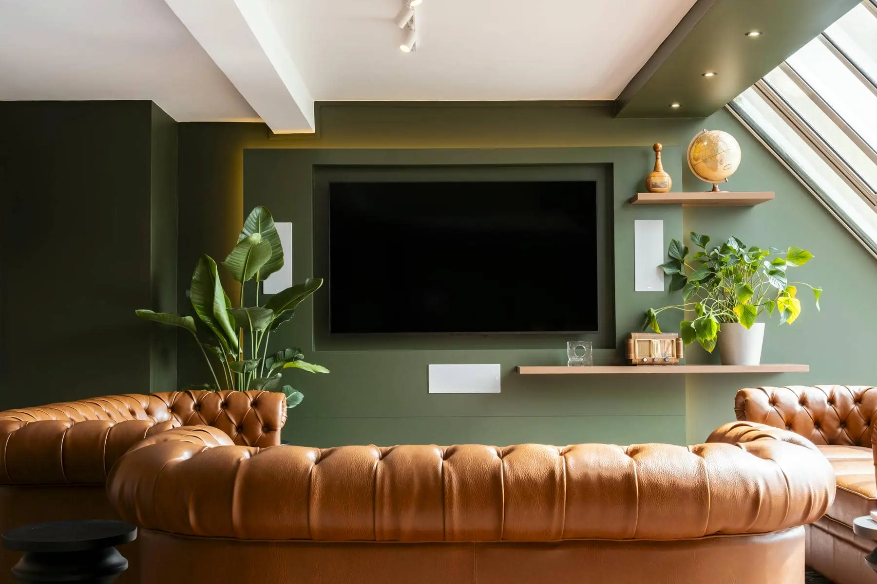 un salon aux murs verts avec un canapé en cuir marron