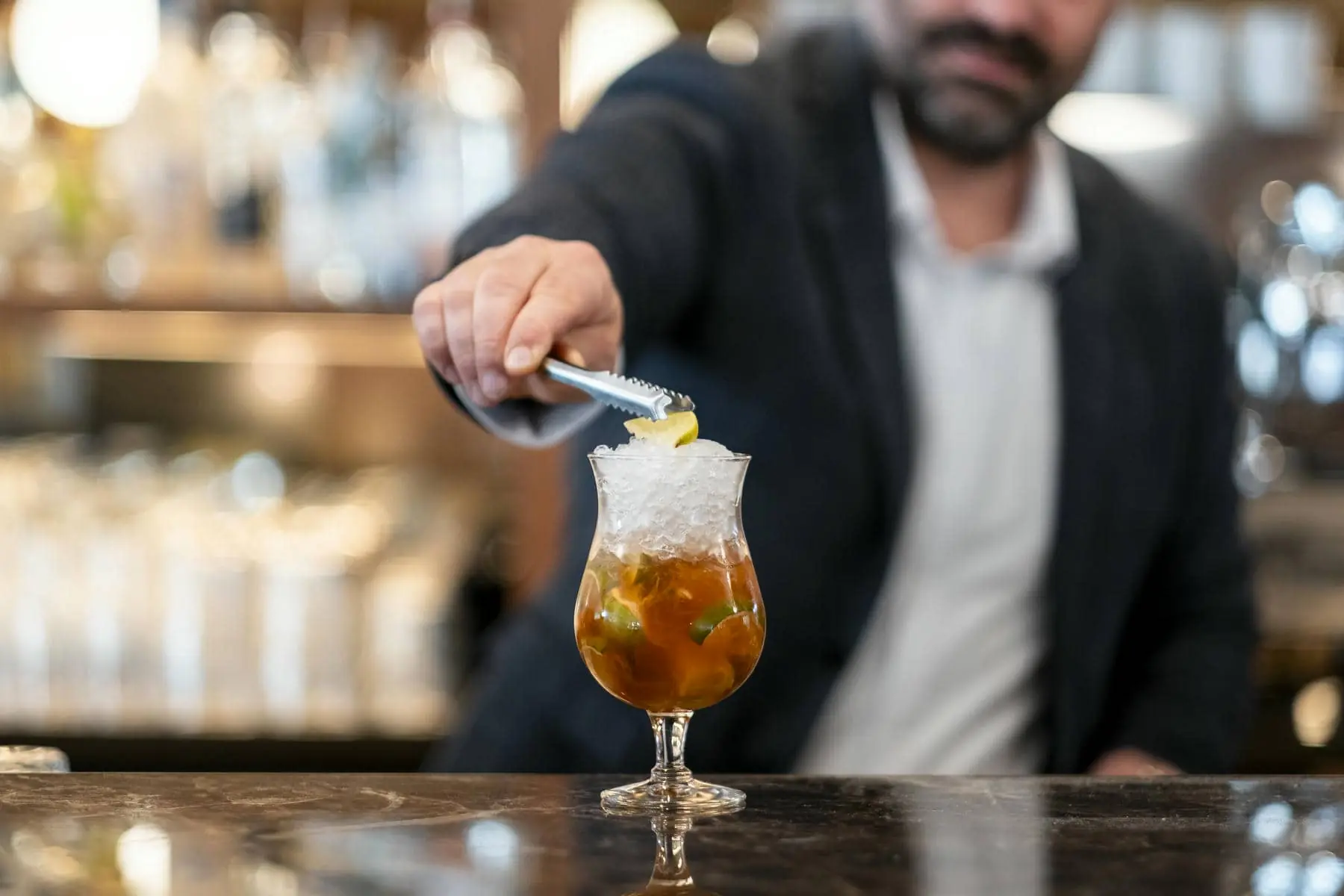 a bartender is adding ice to a drink with tongs