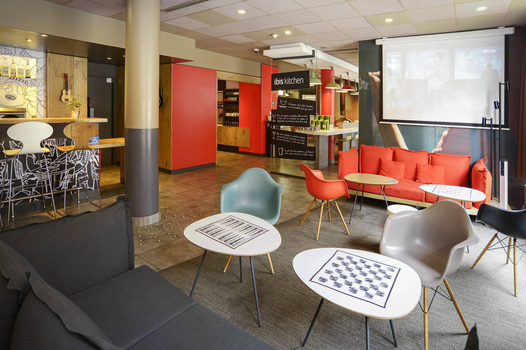 une salle avec des tables et des chaises et un panneau indiquant ibis kitchen