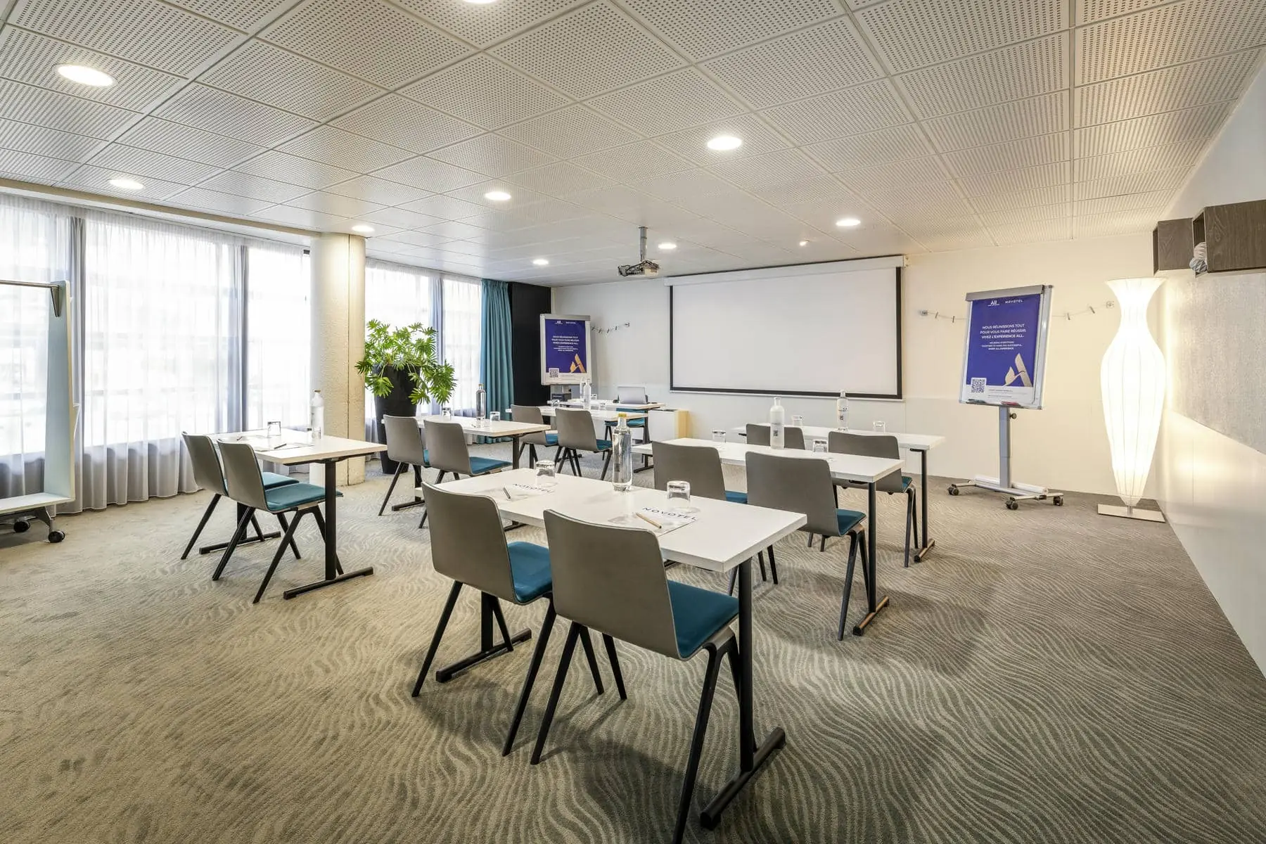 une salle de conférence avec des tables et des chaises et un écran de projection