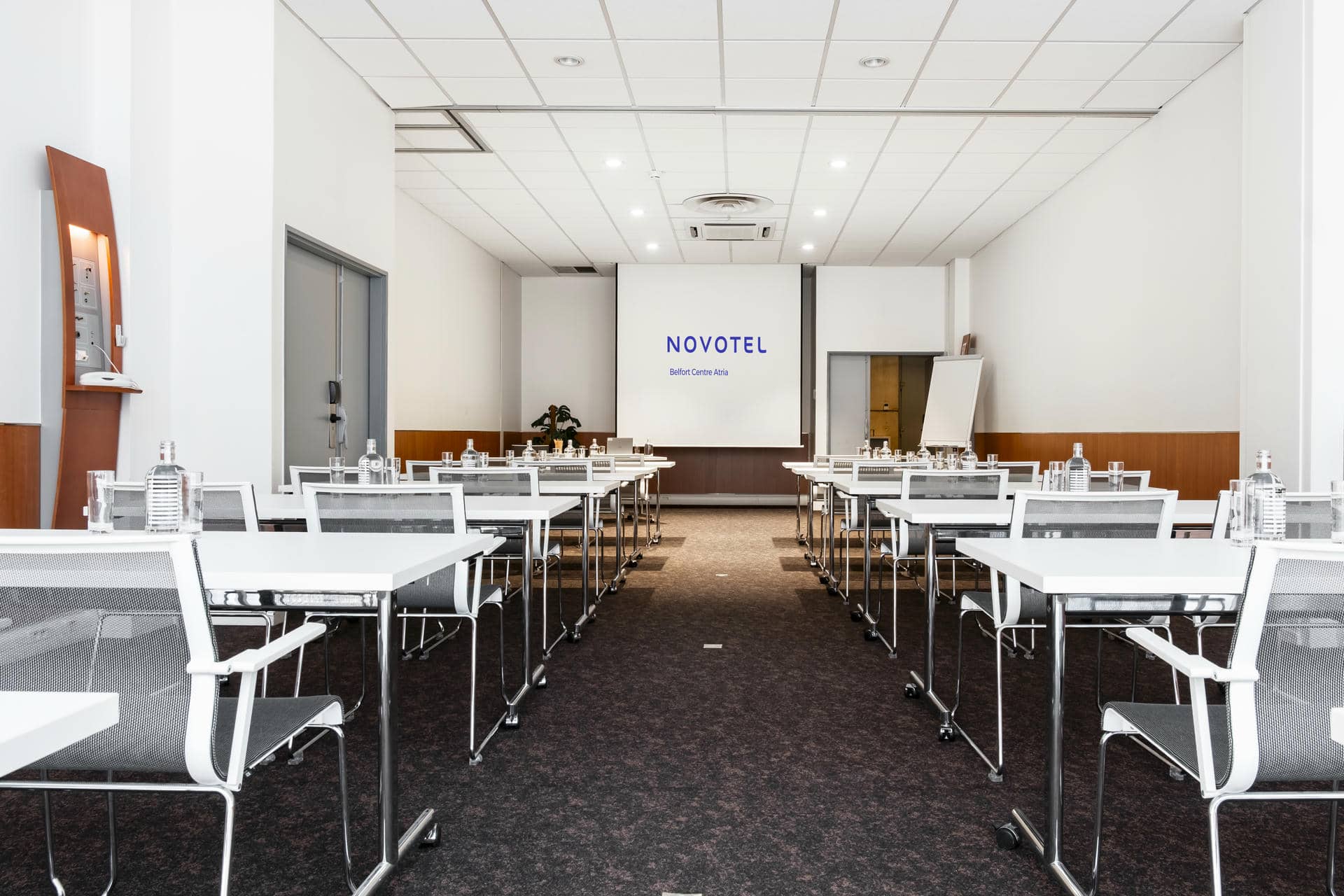 a conference room with tables and chairs and a projector screen that says novotel