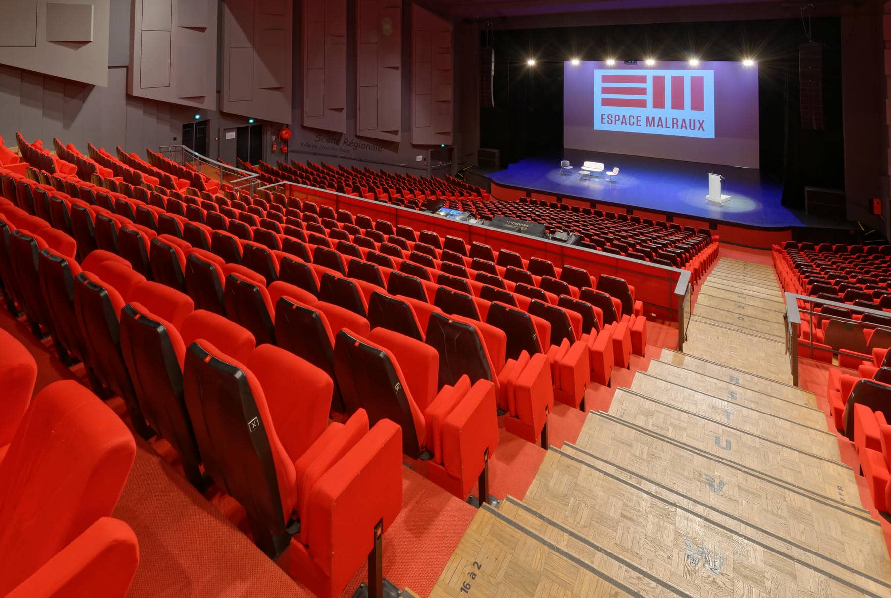 un auditorium avec des sièges rouges et un grand écran sur lequel on peut lire espace mairaux