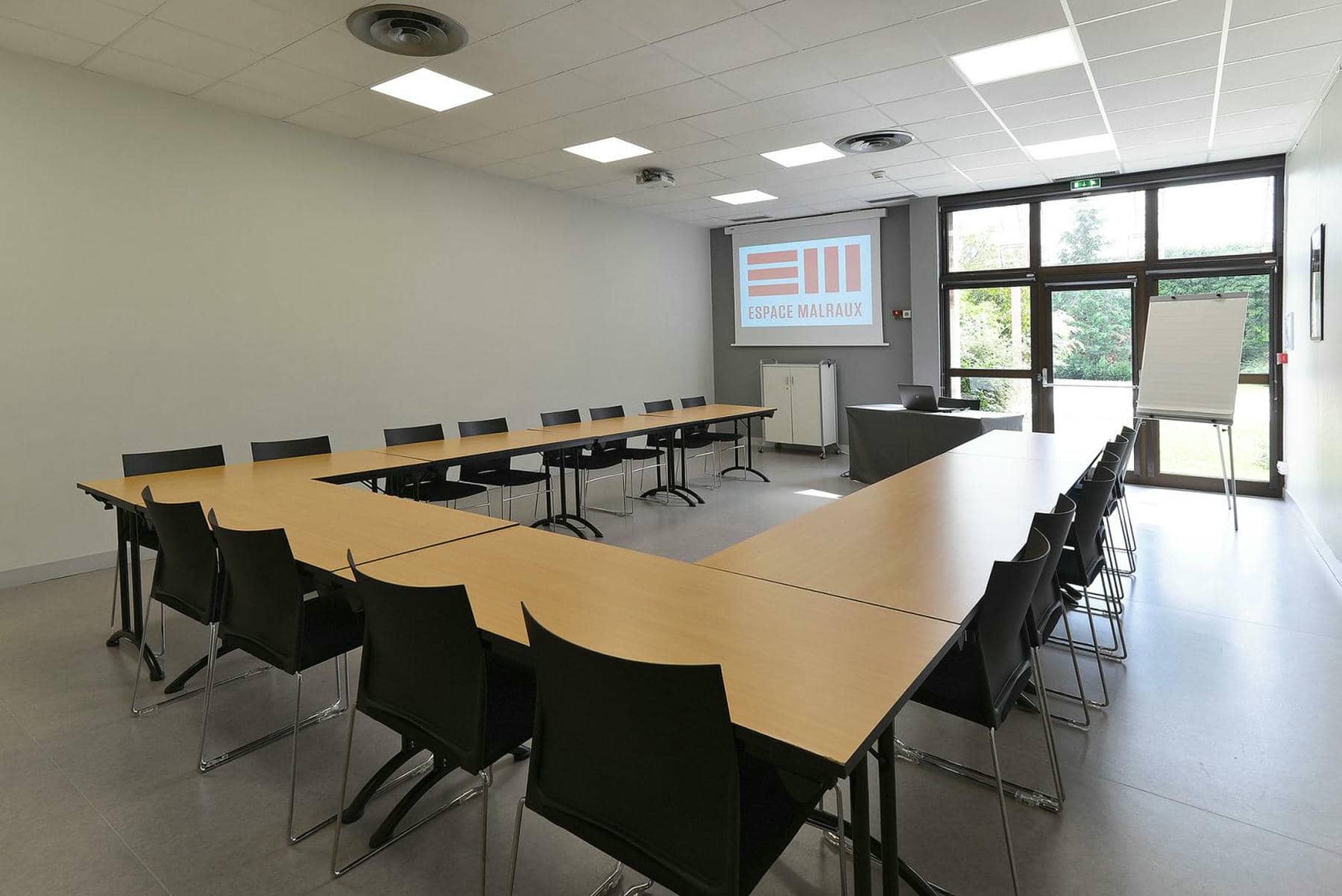 une salle de conférence avec des tables et des chaises et un écran de projection sur lequel est inscrit espace madraux