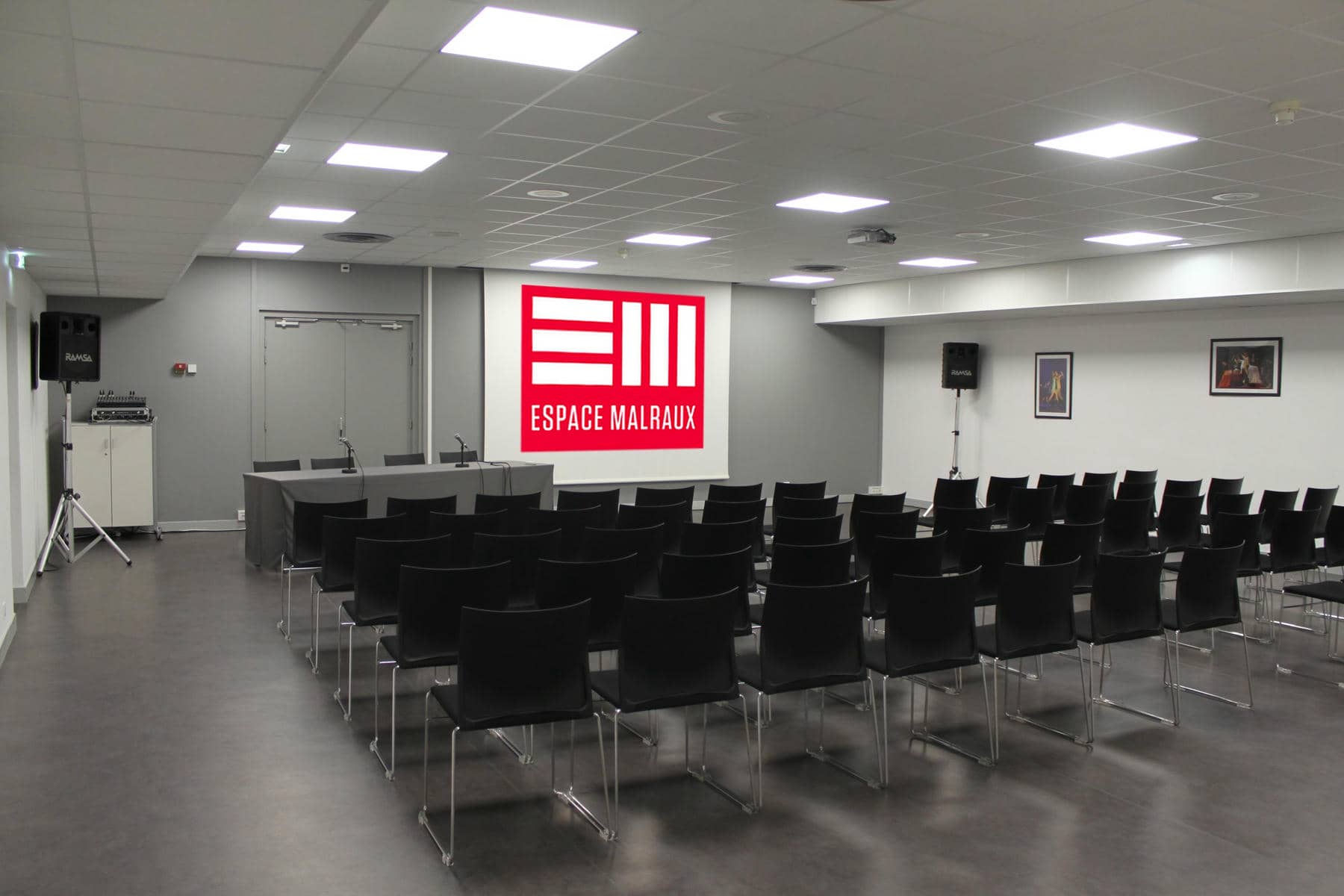 une grande salle avec des rangées de chaises noires et un panneau indiquant espace malraux