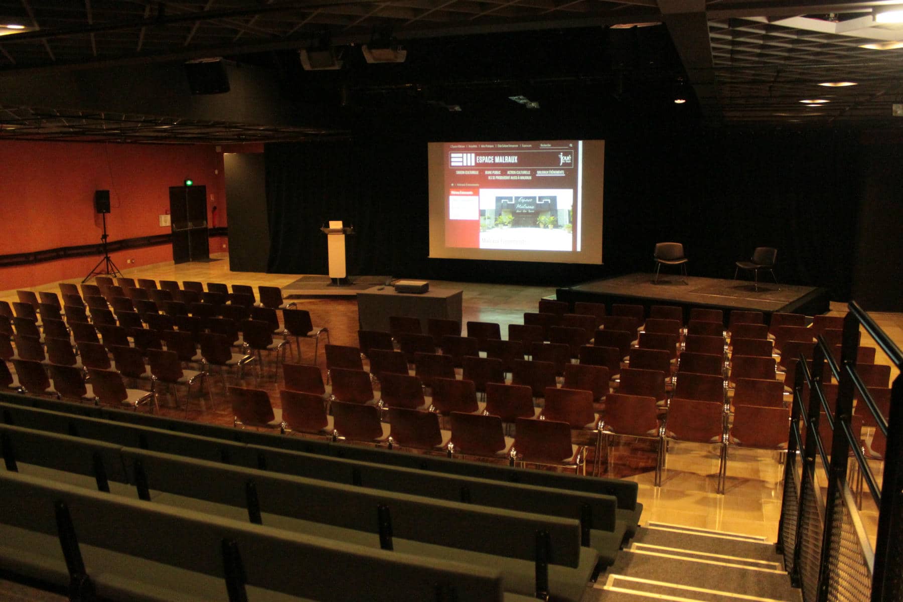 un auditorium avec des rangées de sièges et un écran de projection affichant un site web