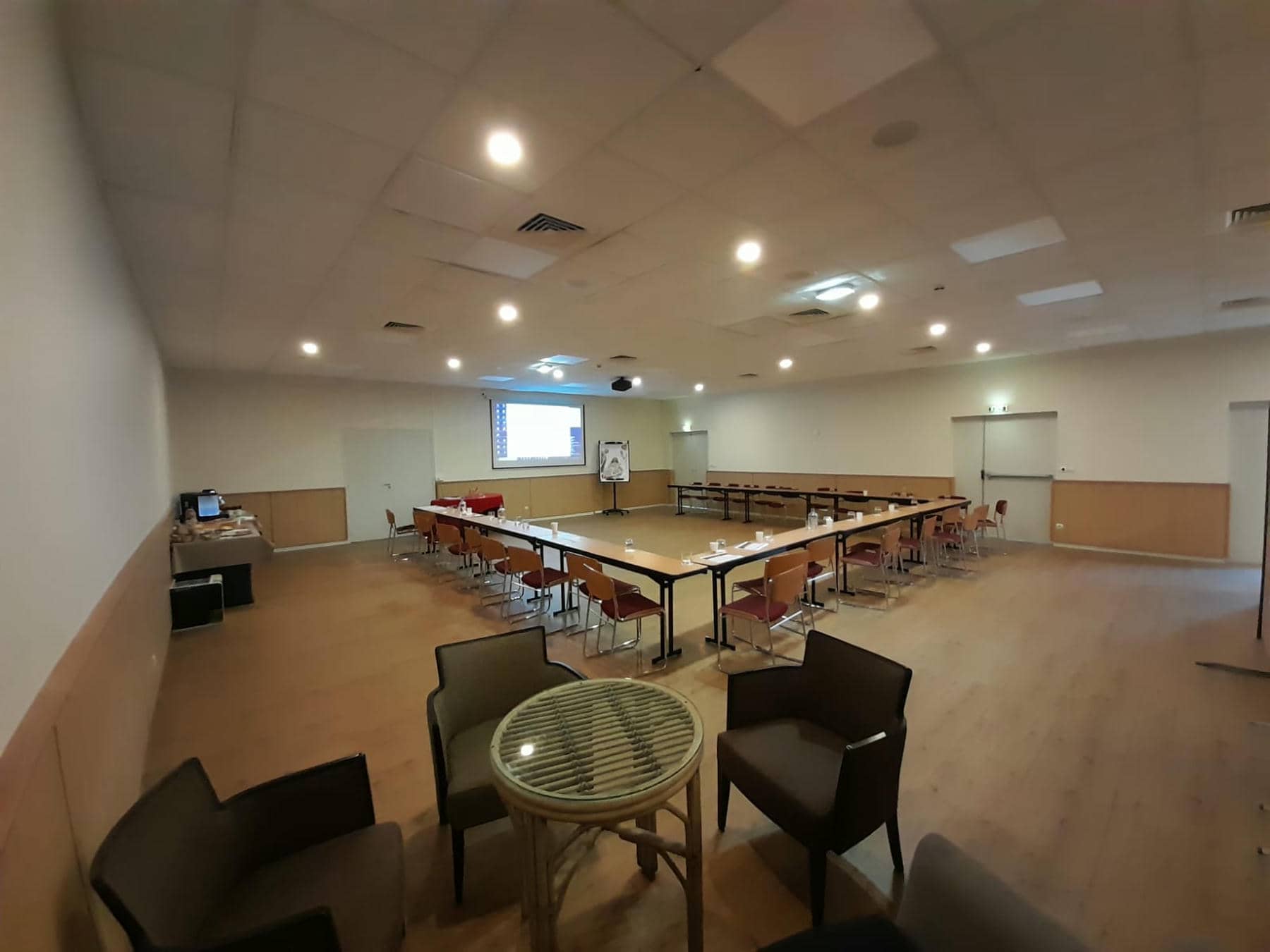 une grande salle avec des tables et des chaises et un écran de projection