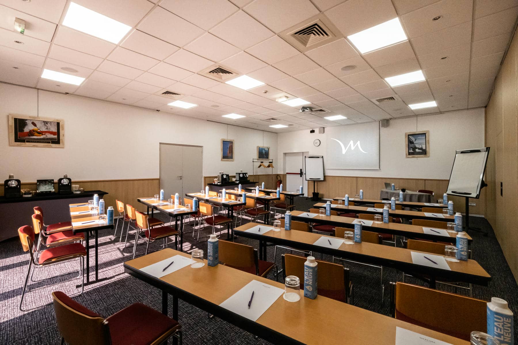 une salle de conférence avec des tables et des chaises et un écran de projection sur lequel figure la lettre m