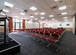 une grande salle avec des rangées de chaises rouges et un podium