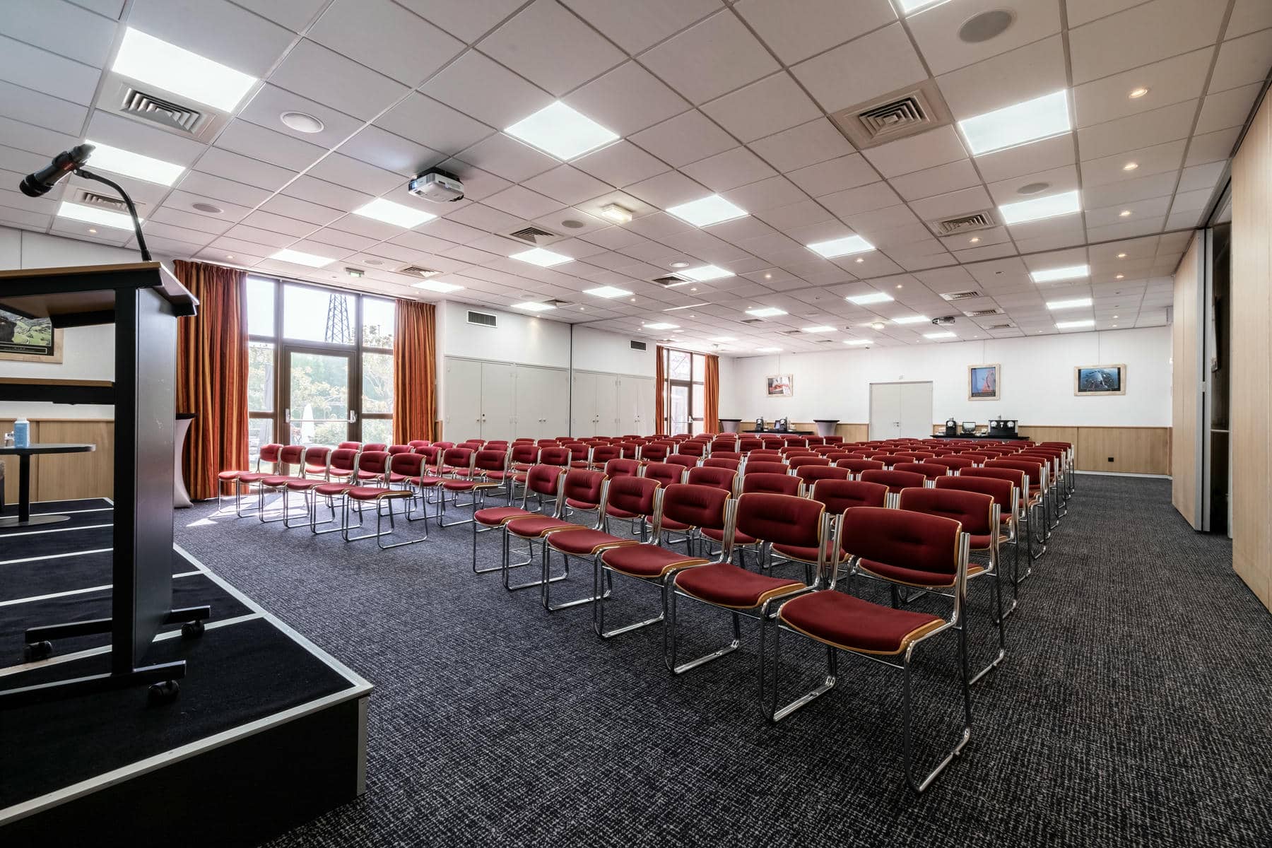 une grande salle avec des rangées de chaises rouges et un podium
