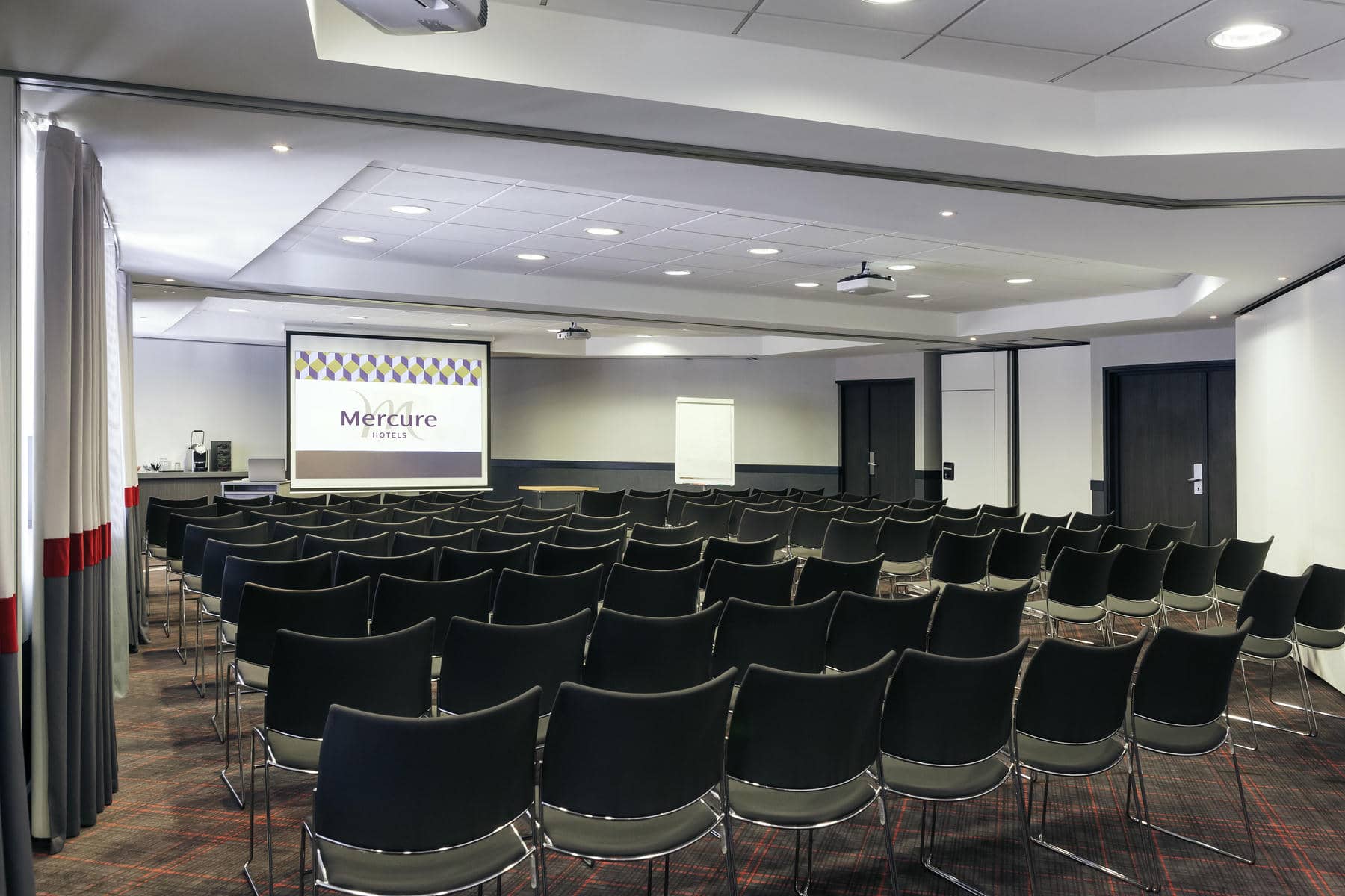 des rangées de chaises noires devant un écran de projecteur mercure