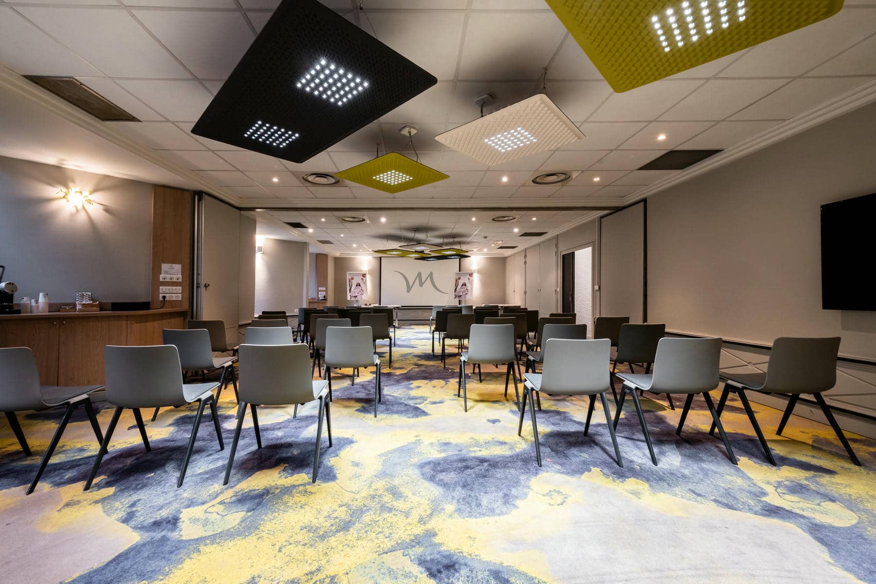 une salle avec des chaises et un écran de projection sur lequel figure la lettre m