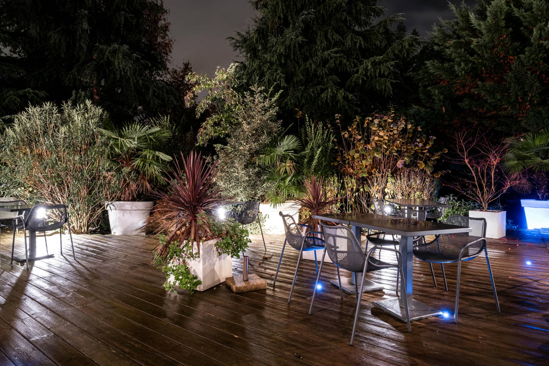 une terrasse en bois avec des tables et des chaises entourées de plantes en pot