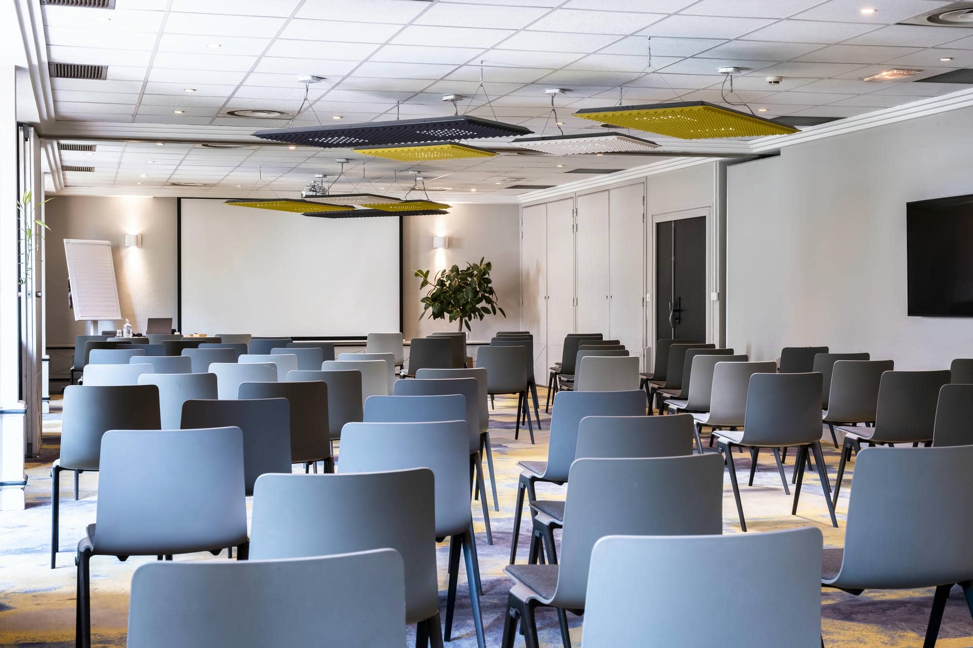 des rangées de chaises devant un écran de projection dans une salle de conférence