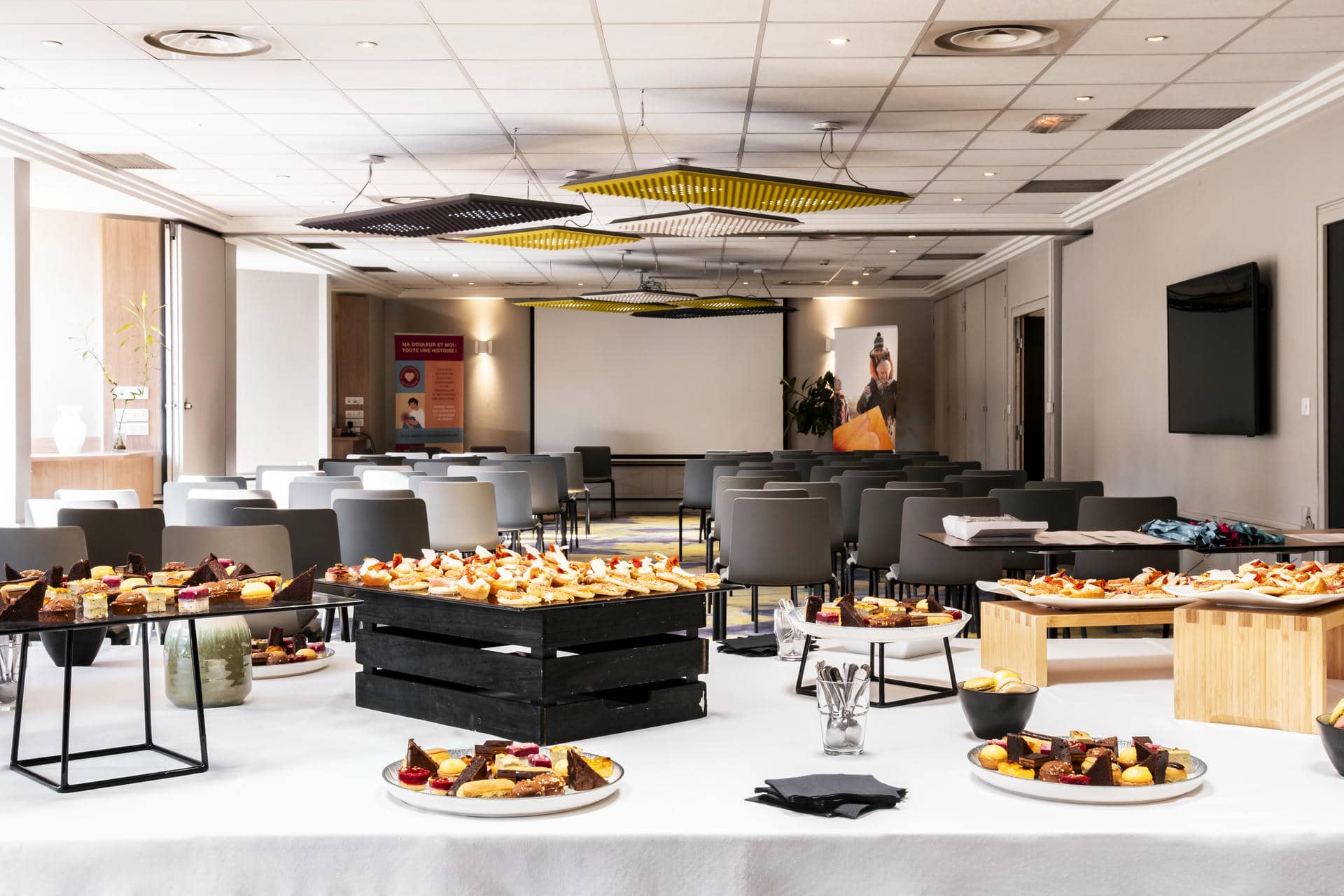 une grande salle avec des tables et des chaises et un écran de projection