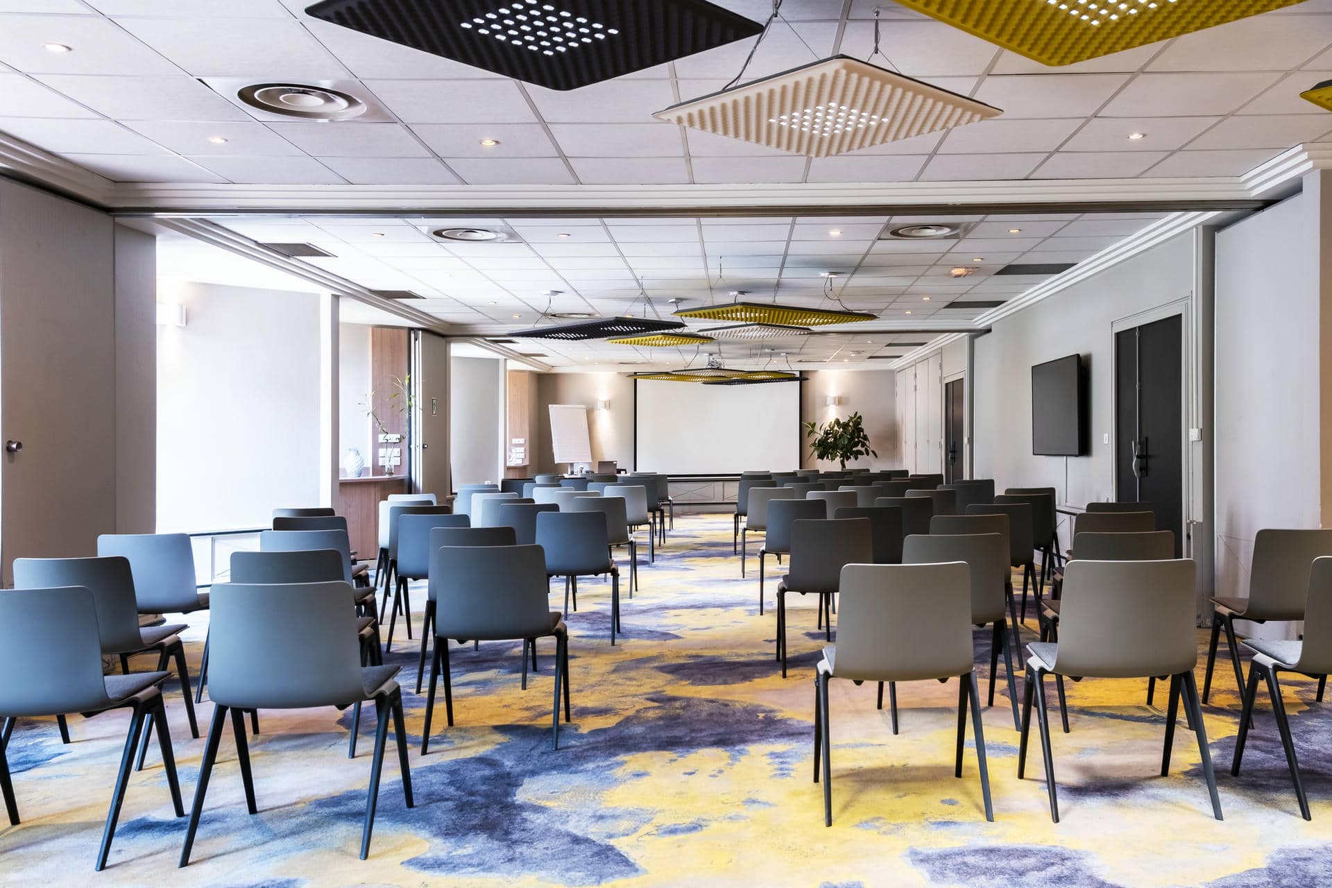 une salle de conférence avec des rangées de chaises et un écran de projection