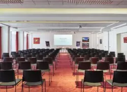 une grande salle avec des rangées de chaises et un écran de projection sur lequel est inscrit mercure